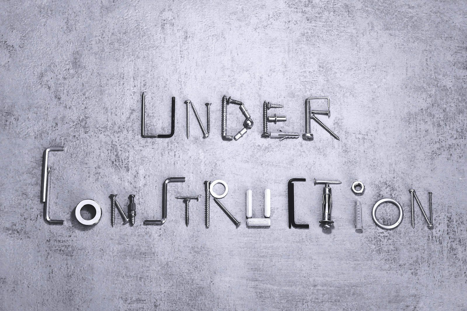 Under construction spelled with metal hardware on a gray background